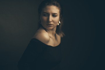 Portrait in the photo Studio of a brown-haired girl, on a black background in black clothes with open shoulders. Short hair.