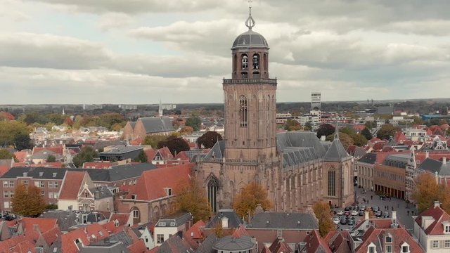 Aerial descend starting high up showing the church in the city centre of the Dutch medieval city of Deventer revealing the boulevard with traffic at the river IJssel that passes by on a cloudy day