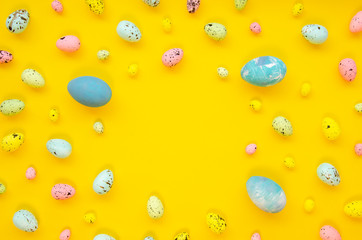 Frame background with decorated quail and chicken eggs with copy space for text. isolated on yellow. Flat lay, top view. Easter card