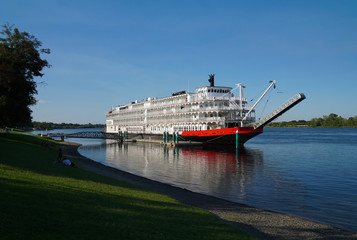A beautiful old paddleboat is docked along a river front park on a lazy summer day.