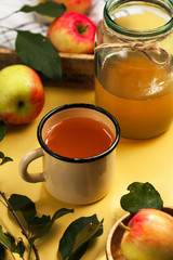Freshly squeezed Apple juice in a mug and in a glass jar surrounded by ripe red and yellow apples.