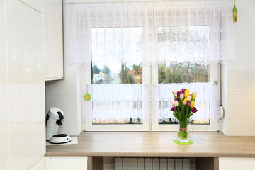 Klorowe tulipany w wazonie na parapecie białego wspłóczesnego okna w jasnej kuchni. - obrazy, fototapety, plakaty