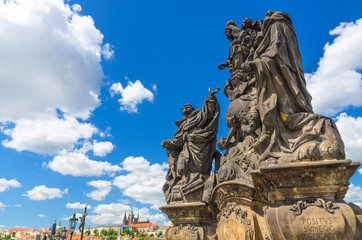 Fototapeta na wymiar Madonna, Ss. Dominic and Thomas Aquinas statue on Charles Bridge Karluv Most over Vltava river with Prague Castle, St. Vitus Cathedral, blue sky white clouds background, Bohemia, Czech Republic