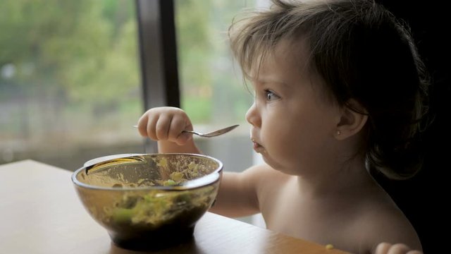 Adorable toddler girl eating healthy oatmeals with avocado and kiwi for breakfast