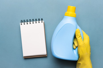 Detergent bottle in female hand and blank page notebook over blue background. Washing tips template.