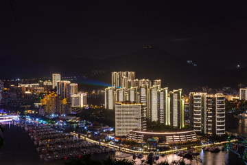 Naklejka premium Night view of Sanya city with bright multi-colored illumination buildings, structures, roads, sidewalks, poles, bridges.