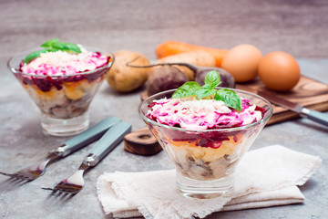 Traditional Russian appetizer of boiled vegetables and fish - herring under a fur coat in bowls and ingredients for cooking on the table. Russian salad