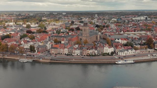 Aerial zooming in on waterfront traditional historic waterfront facades of houses in the city centre of medieval Deventer with large church behind and river IJssel passing by in the foreground