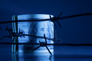 Economic warfare, sanctions and embargo busting concept. US Dollar banknotes wrapped in barbed...