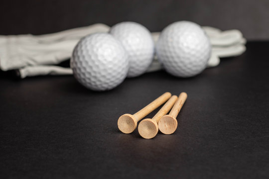 Golf ball tee&rsquo;s in front of golf balls and gloves illustrative photo shot on black studio background isolated recreational sport equipment for golf courses and leisure, hobbies and retirement. 