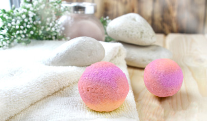 Fototapeta na wymiar Spa or wellness bodycare setting. Still life image with bath bombs, stones, scrub, towel on wooden background. Spring or summer relax concept.