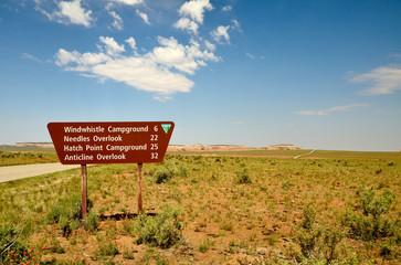 brown road sign indicating the distance to different destinations, in the background blue sky with white clouds.