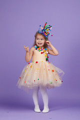 Children's birthday party, masquerade. Little happy toddler child girl in a puffy tutu fancy dress, having fun on Violet background. Space for text