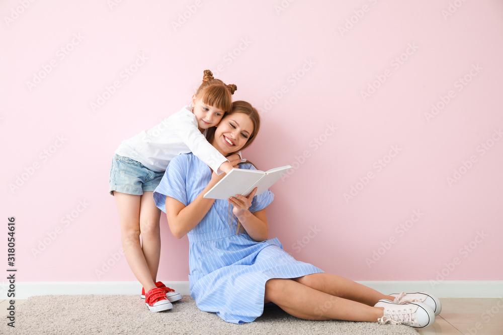 Wall mural beautiful young woman and her little daughter reading book near color wall