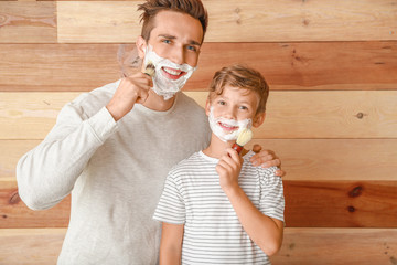 Father with son applying shaving foam onto their faces against wooden background