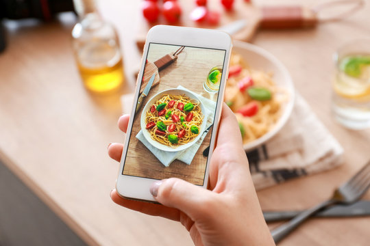 Female food photographer with mobile phone taking picture of pasta