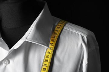 Mannequin with custom tailored shirt and measuring tape on dark background, closeup