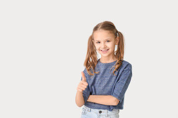 Fototapeta premium Cute little girl showing thumb-up gesture on white background