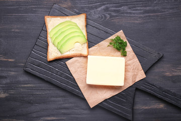 Fresh butter with bread and avocado on dark table