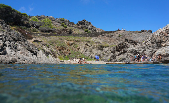 Mediterranean sea summer vacation, small rocky beach with tourists seen from water surface, Spain, Costa Brava, Cap de Creus, Catalonia, Cala Culip