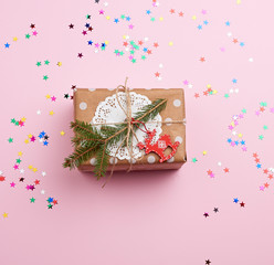 rectangular box wrapped in brown kraft paper and tied with a rope lies on a pink background