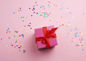 beautiful pink closed box with a big bow on a pink background with multi-colored sparkles