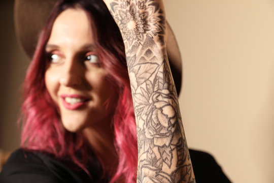 Beautiful woman with tattoos on arm against beige background, focus on hand