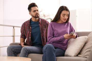 Obraz premium Distrustful young man peering into girlfriend's smartphone at home