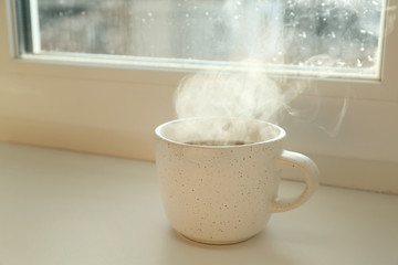 Cup of hot drink near window on rainy day