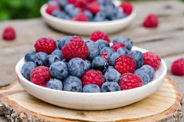 Still life with a blueberries and raspberries on an old wooden table, at the garden. Rural natural food style.