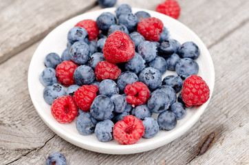 Still life with a blueberries and raspberries on an old wooden table, at the garden. Rural natural food style.