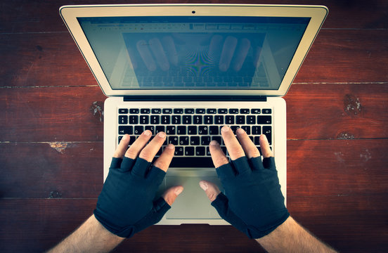 look down to the males hands with gloves typing on laptop keyboard on the red wood background. Background of working space.