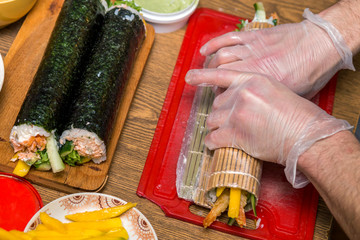 Process of making sushi and rolls. Close-up of man chef hands preparing traditional Japanese food at home or in restaurant on kitchen table.