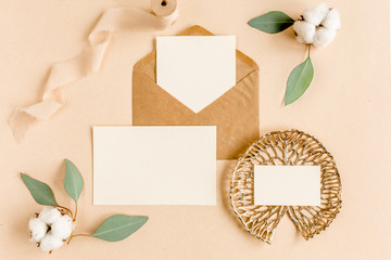 Mockup invitation, blank greeting card and craft envelope, green leaves eucalyptus. Flat lay, top view.