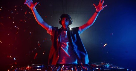 Cool dj standing at a mixer controller composing a dance music list, dancing while spotted by nightclub colorful lights - nightlife concept 4k footage - Powered by Adobe
