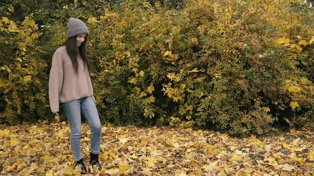 Happy girl has enjoyment in autumn park, whirls and undresses cap