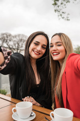 Two young friends taking a selfie together at coffee shop.