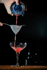 Bartender in a bar mixing alcoholic cocktail. A professional bartender at work in a bar pours a red drink into a glass at a nightclub party.