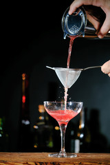 Bartender in a bar mixing alcoholic cocktail. A professional bartender at work in a bar pours a red drink into a glass at a nightclub party.