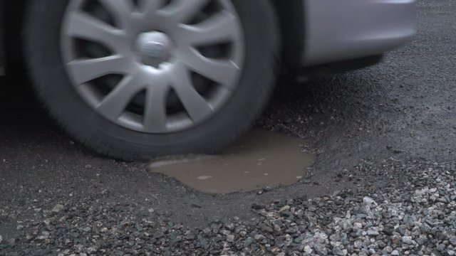 Vehicle driving over a damaged road with a Pothole in the street. Side View of Wheel