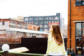 Fototapeta na wymiar beautiful teen girl long-haired teenager in yellow clothes on the background of the cityscape on the roof of the house