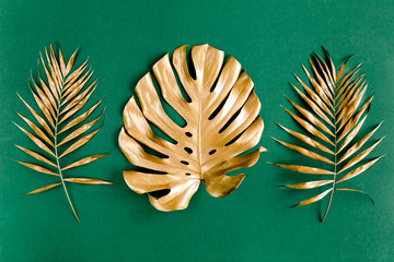 Set of gold tropical palm leaves Monstera on green background. Flat lay, top view minimal concept.