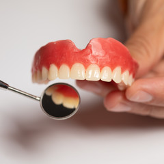 Fototapeta na wymiar Denture prosthesis in doctor dentist hands, checking with mirror
