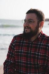 portrait of smiling young man with red shirt, beard and glasses