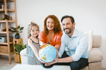 Smiling parents and daughter holding globe, planning vacation.