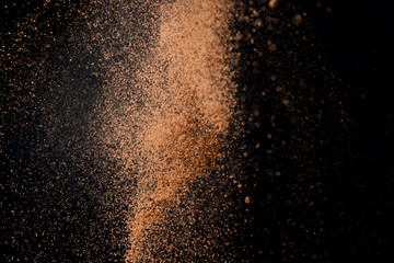 Cocoa powder explosion in motion on black background. Chocolate dust.