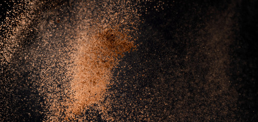 Cocoa powder explosion in motion on black background. Chocolate dust. Wide banner.