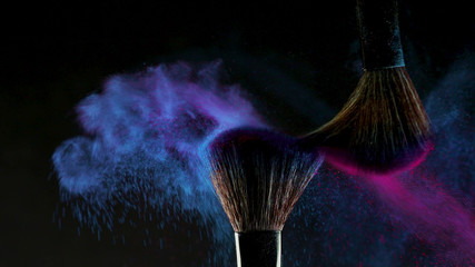 Two Soft cosmetic brushes release a cloud of colored smoke from bright eyeshadow and powder, - obrazy, fototapety, plakaty