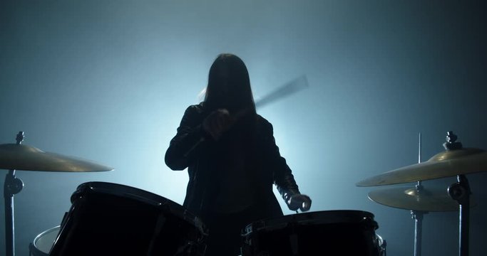 An authentic drummer playing a solo in a band, hitting the drums while playing rock or metal music, silhouetted on smoked stage - band, music concept 4k footage