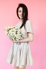 Girl in a dress with a bouqet of flowers chamomile on a pink background in front of camera